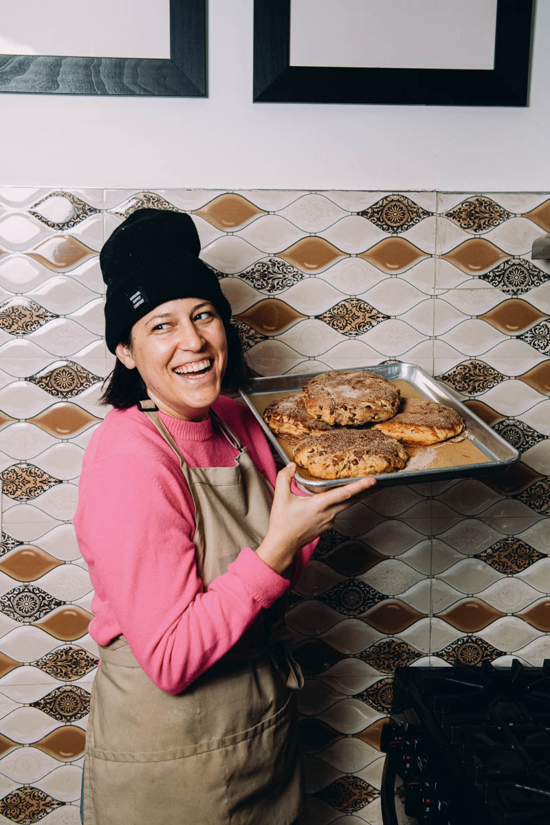 Wandel Founder Stephanie Berlin holds a sheet pan of Wandel bread loafs over stove with a big smile.